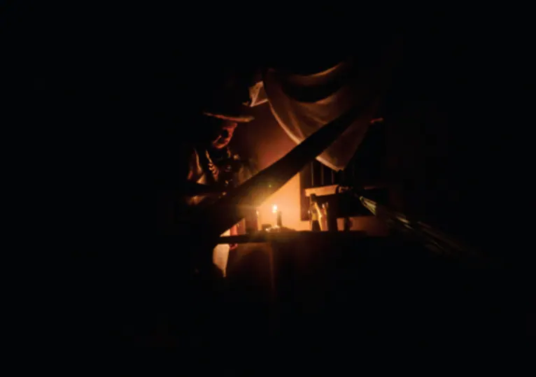 Escena nocturna con una vela encendida bajo un techo (Kinchachingapa, cierre espiritual del territorio).