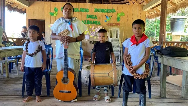 Mayor con guitarra y tres niños con bombo y collares de semillas en el salón (corte del pelo Agcha Rutui).