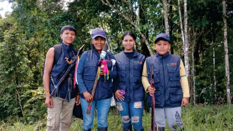 Cuatro jóvenes de la guardia (Wasikamas) con chalecos y bastones en la selva (gobierno propio).