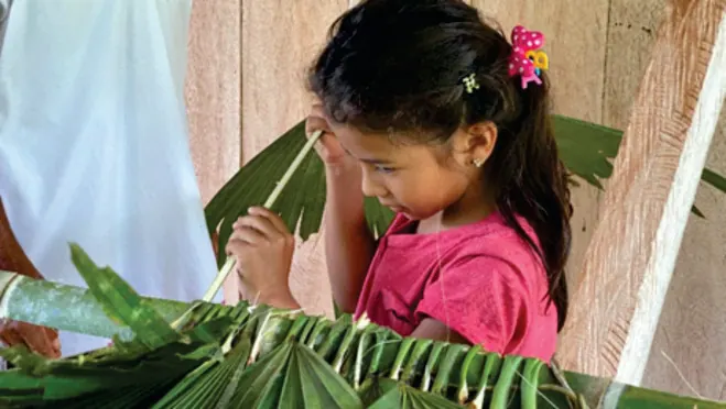 Niña tejiendo una hoja de palma (modelo educativo propio).