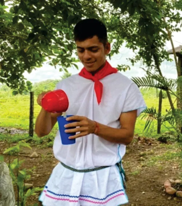 Joven con cusma blanca y pañuelo rojo sirviendo bebida en un vaso (economías propias).