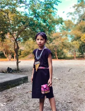 Niña con vestido negro, collares y mochila de pie en un terreno abierto (Niños y niñas).
