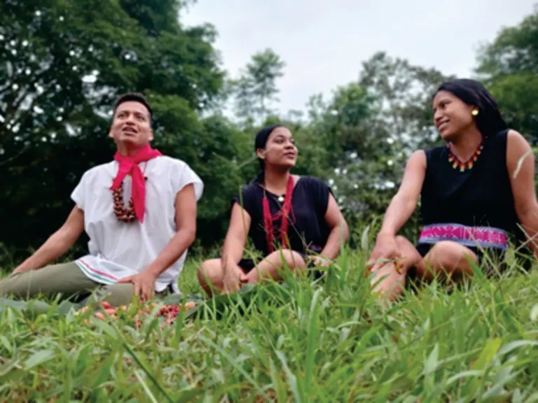Tres jóvenes con vestido tradicional sentados en la hierba (Jóvenes).
