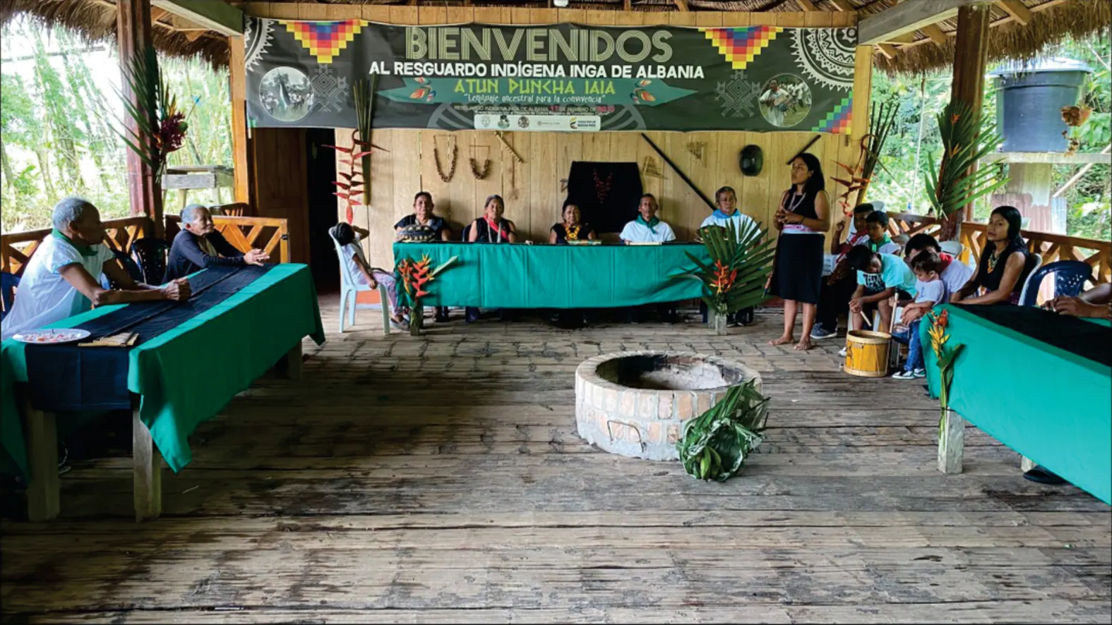 Interior del tambo con mesas verdes, tulpa al centro y letrero de bienvenida, durante una reunión (Jóvenes, Fondo de Educación).