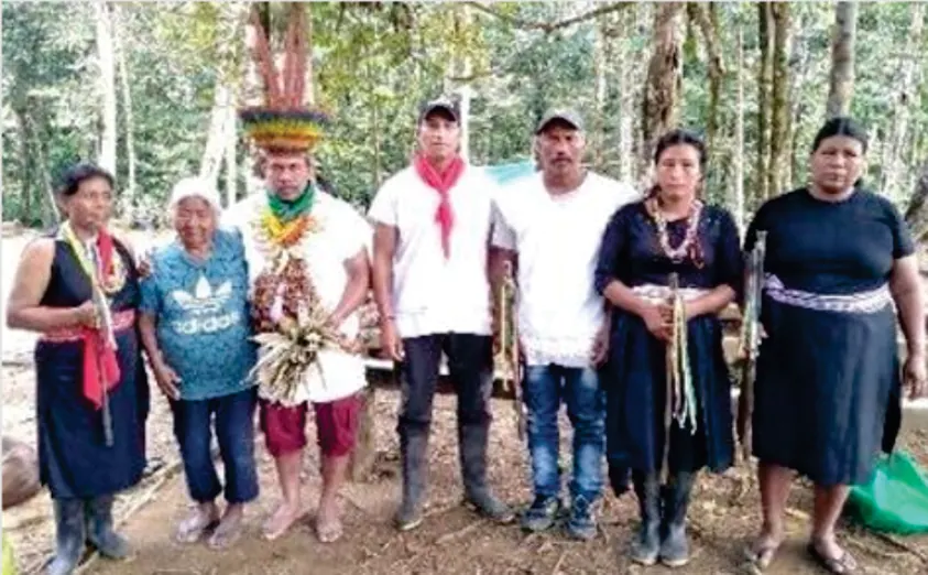 Siete personas de la comunidad en el bosque, una con corona de plumas y collares, y mujeres con traje propio.