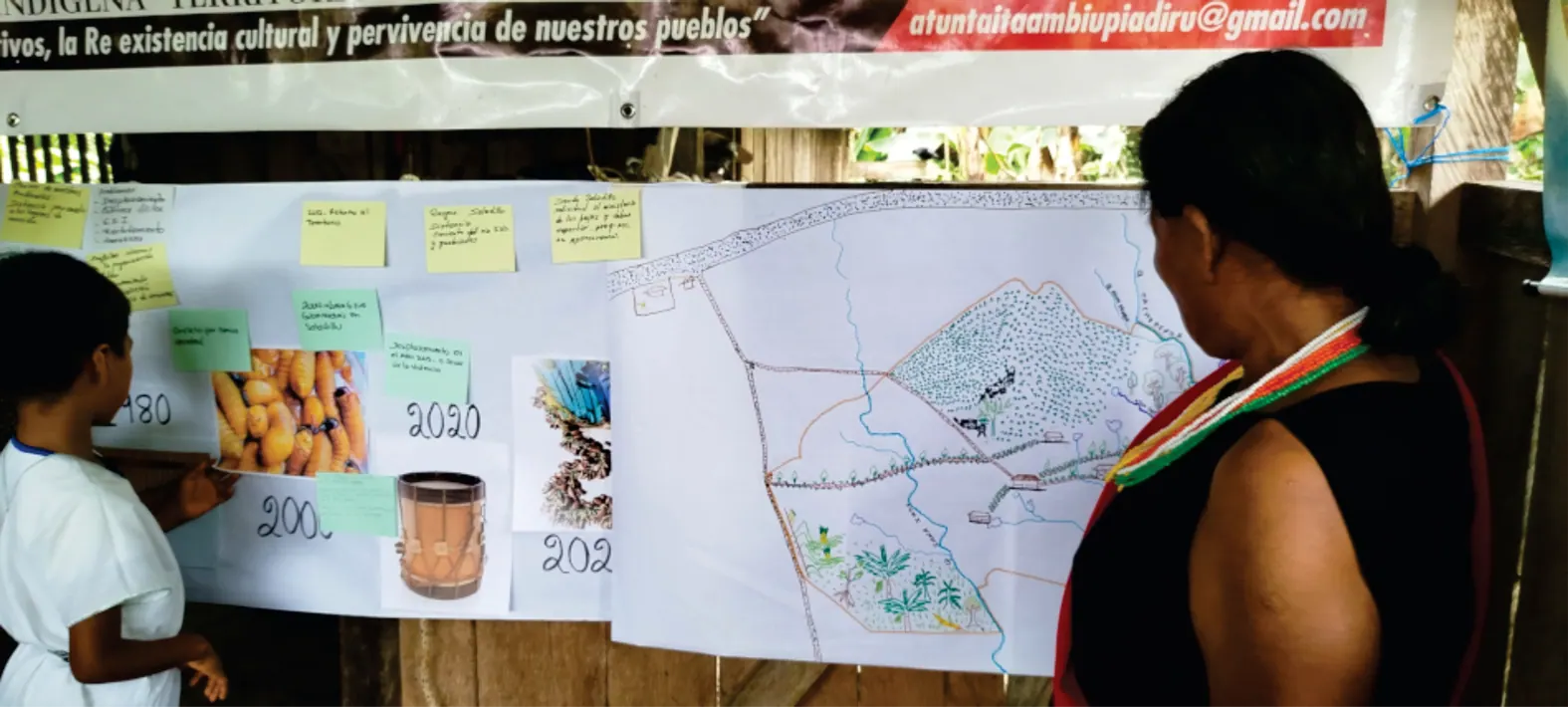 Mujer de la comunidad explicando carteleras y un mapa dibujado en papelógrafos durante la minga del Plan de Vida.