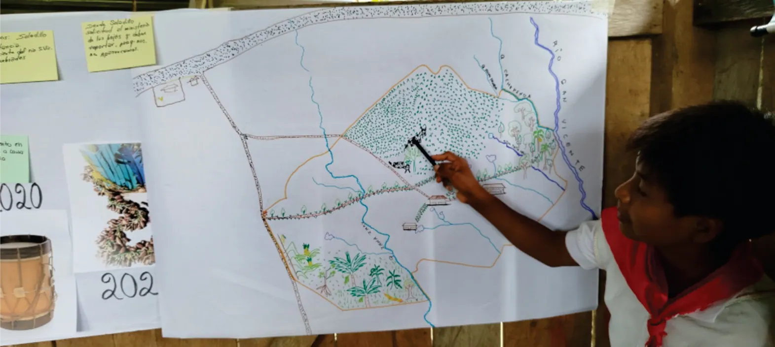 Joven con pañoleta roja que dibuja sobre un mapa en papelógrafo (cartografía social) durante la minga.