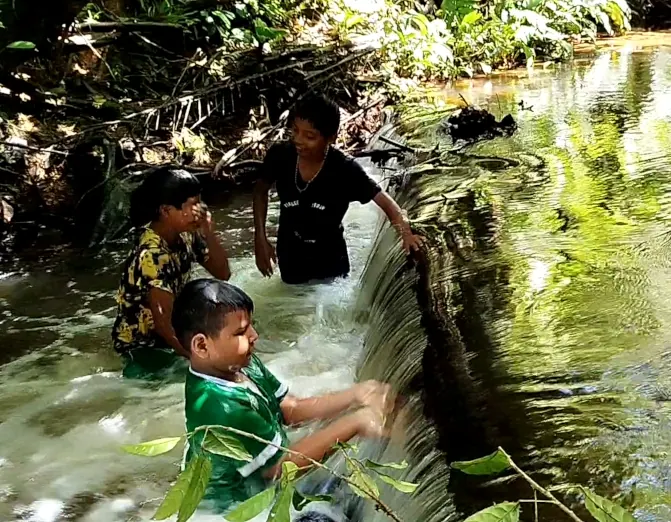 Niños y una mujer dentro de una quebrada, junto a una pequeña caída de agua.