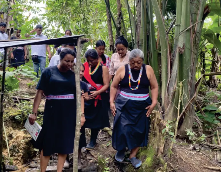Mujeres con traje propio caminando por la chagra entre plantas.