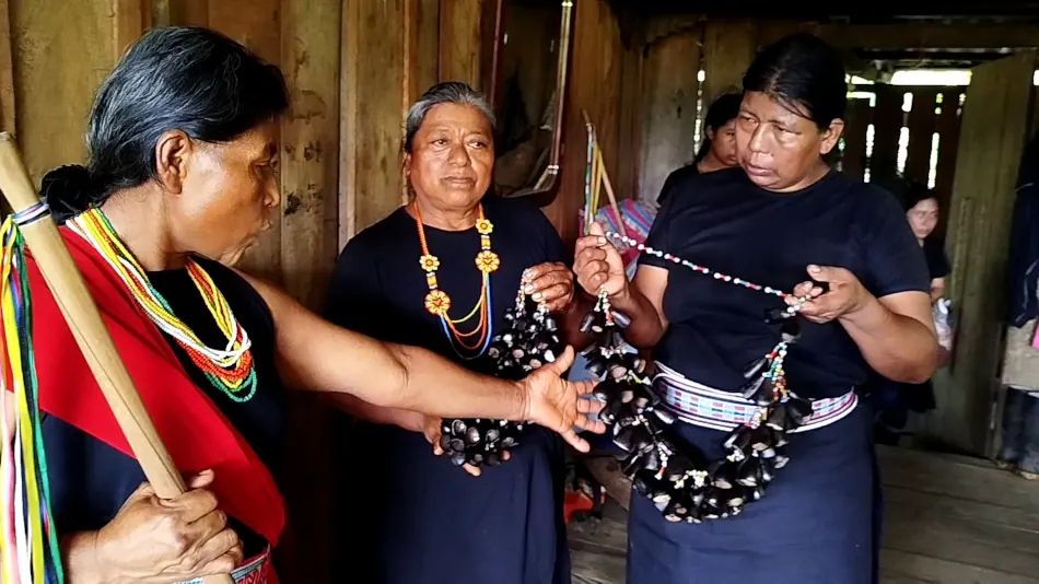 Mujeres con traje propio mostrando collares de semillas (artesanía).