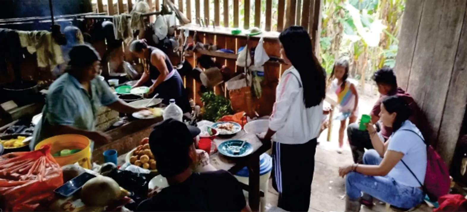 Cocina comunitaria con personas alrededor de una mesa con alimentos.
