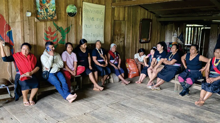 Mujeres sentadas en una reunión dentro de una casa de madera (registro fotográfico).