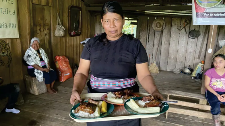 Mujer con traje propio que sirve una bandeja con alimentos (registro fotográfico).