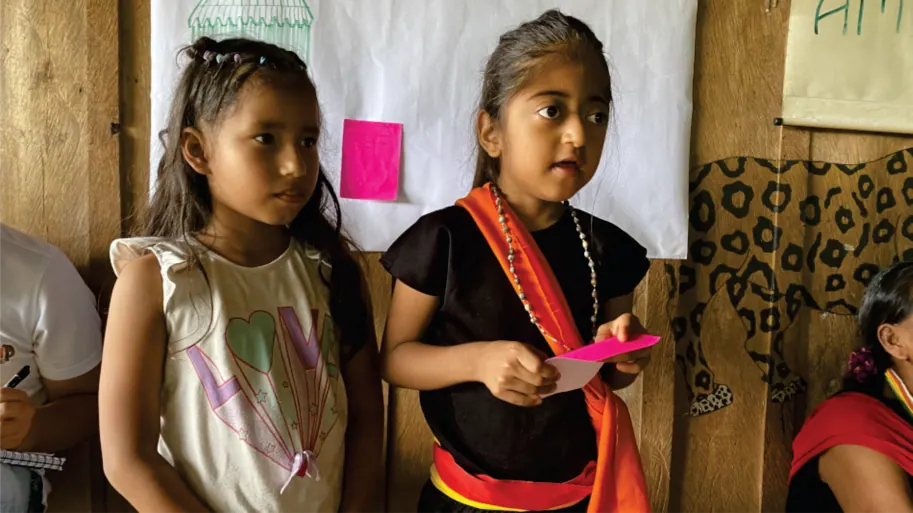 Niñas con traje propio, una con una cartulina rosada (registro fotográfico).
