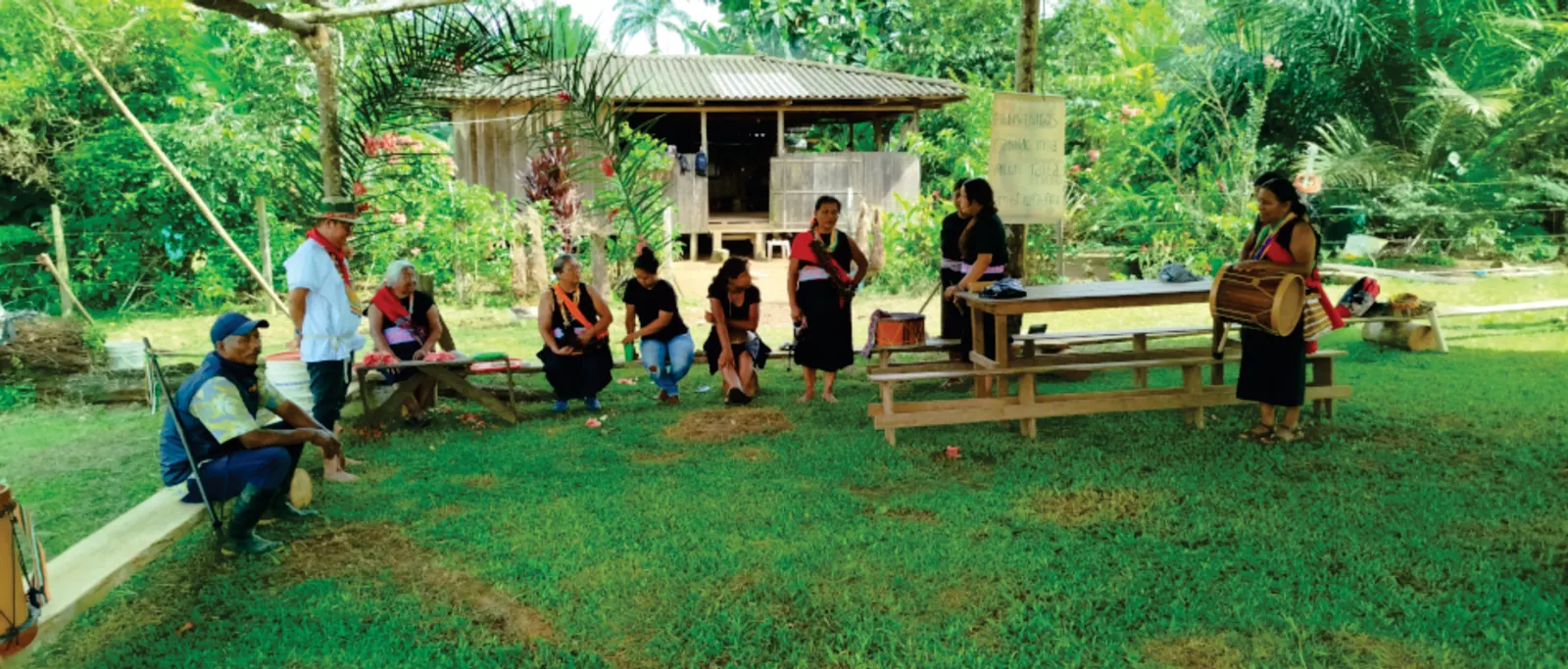 Personas reunidas en el patio frente a una casa de madera (registro fotográfico).