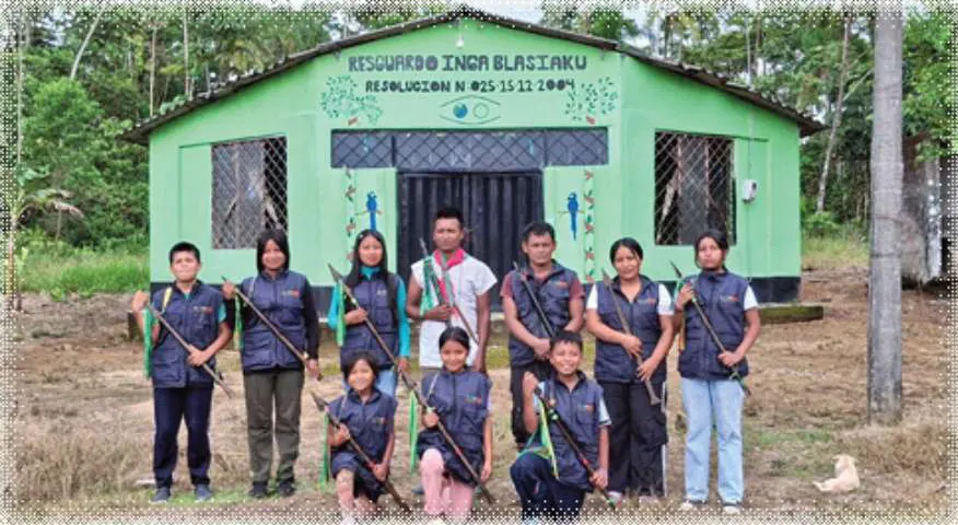 Grupo de la guardia indígena con chalecos y bastones frente a la casa verde del «Resguardo Inga Blasiaku, Resolución N° 025 15 12 2004».