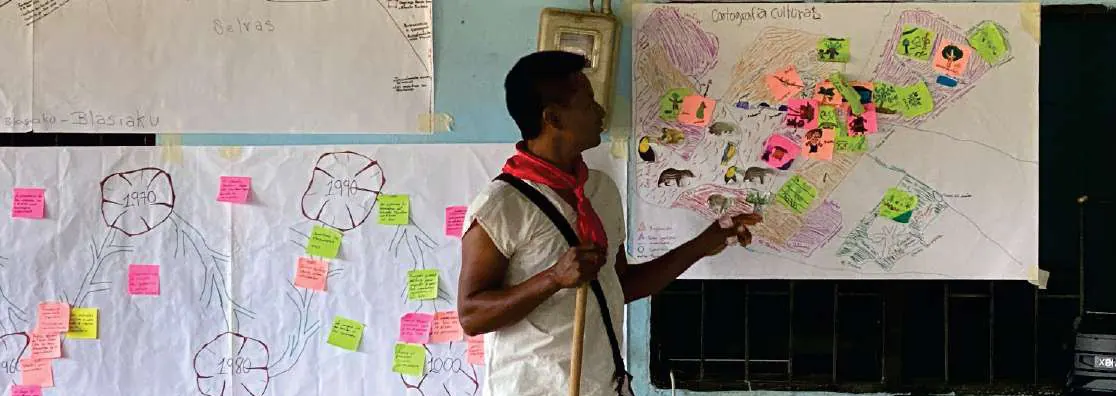 Hombre con pañoleta roja que explica una cartografía social en papelógrafos con notas adhesivas.