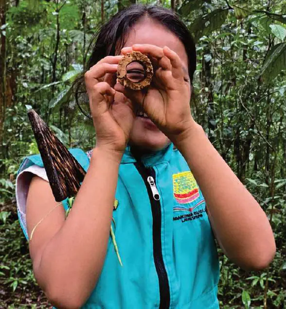 Niña con chaleco de la guardia que mira a través de un objeto circular, en el bosque.