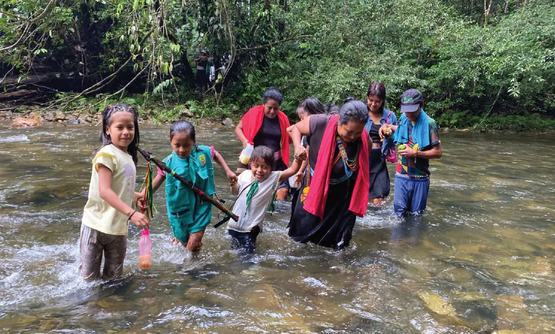 Niños y mujeres que cruzan un río, una mujer con chal rojo.