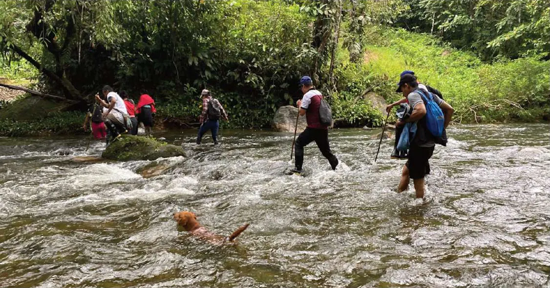 Personas cruzando un río pedregoso durante un recorrido.