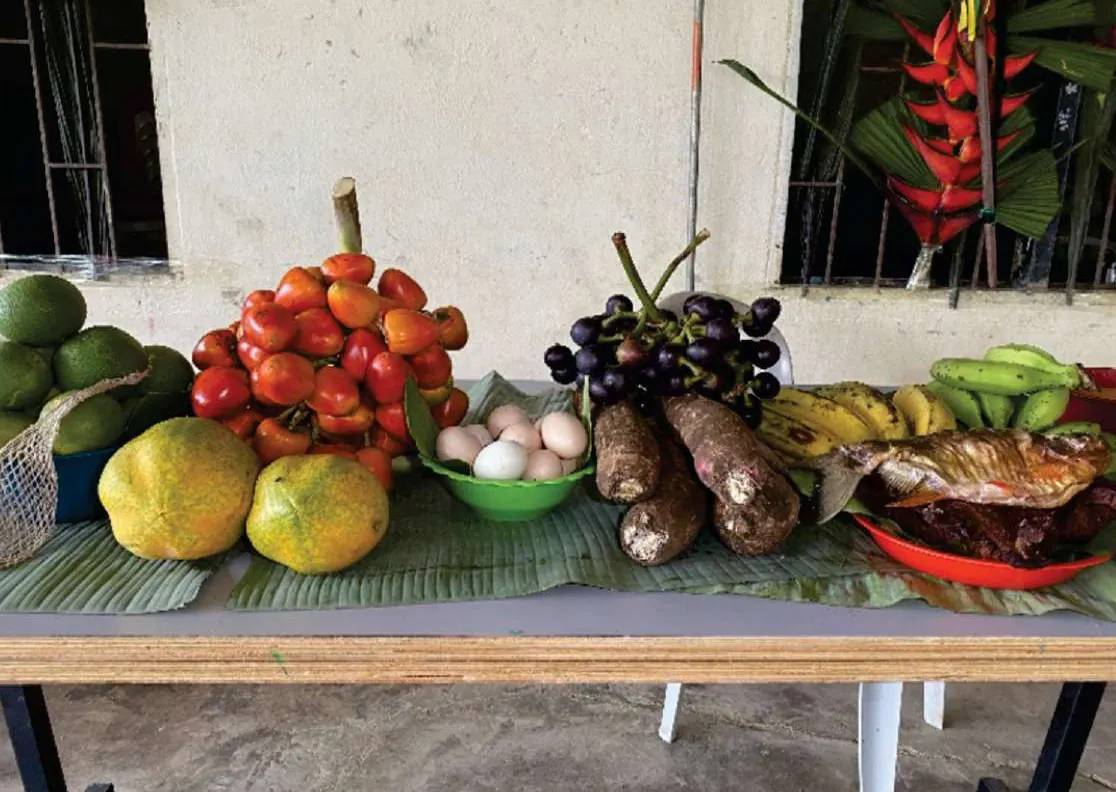 Mesa con alimentos del territorio: papayas, chontaduro, uvas de monte, yuca, huevos, plátano, pescado y heliconias.