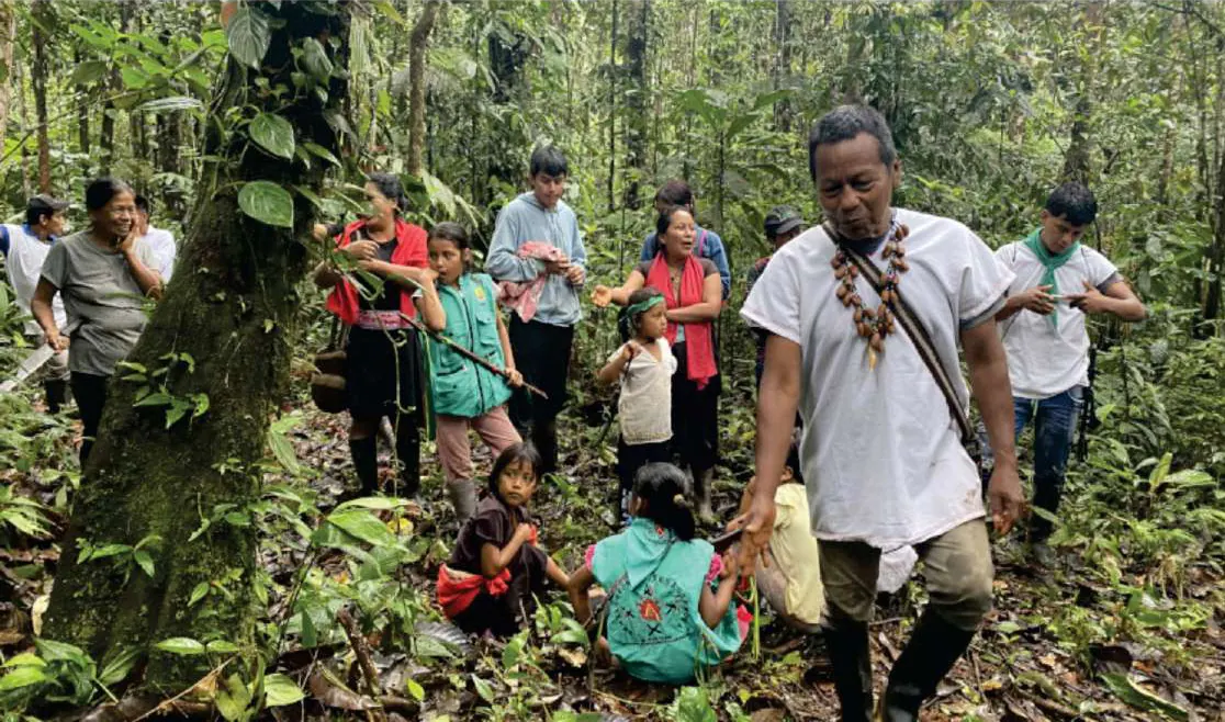 Mayor con collares que guía un recorrido por el bosque con niños y adultos.