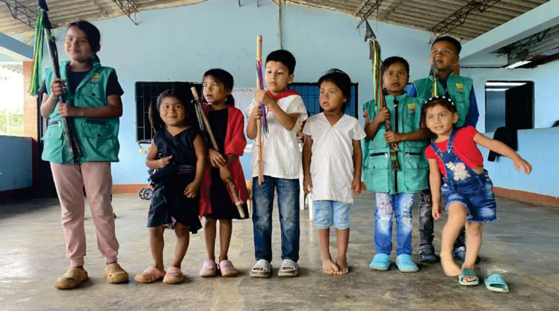 Niños con traje propio y chaleco de la guardia, con bastones, en un salón de la escuela.