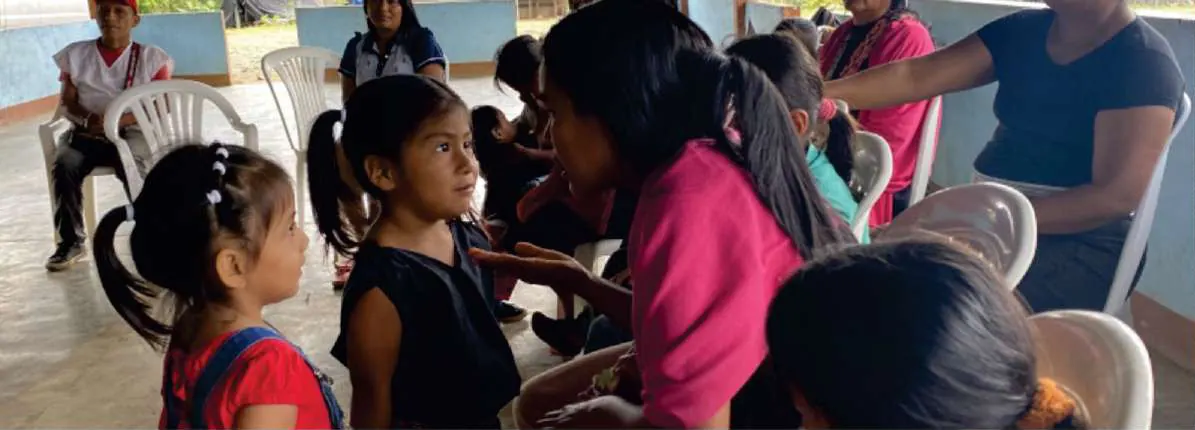 Niñas y mujeres sentadas en una actividad dentro de la caseta comunal.