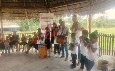 Niños y adultos que tocan flautas y tambores bajo un tambo.
