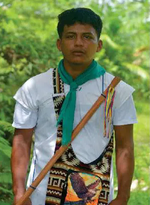 Joven con traje propio: camisa blanca, pañoleta verde, mochila tejida y lanza.