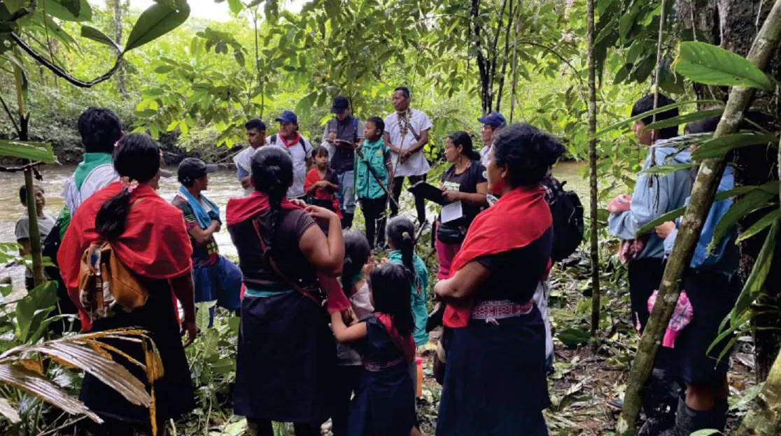 Mujeres con chal rojo y niños reunidos en el bosque.