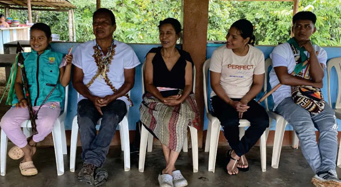 Mujeres y un hombre sentados en una reunión en la caseta comunal.