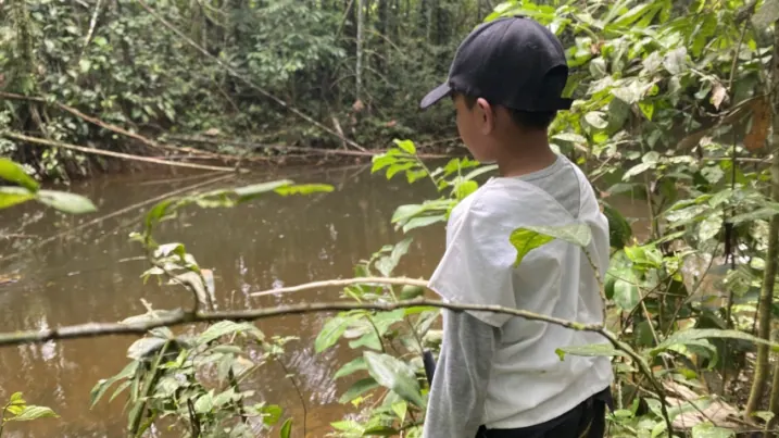 Joven con gorra que observa una quebrada en el bosque.