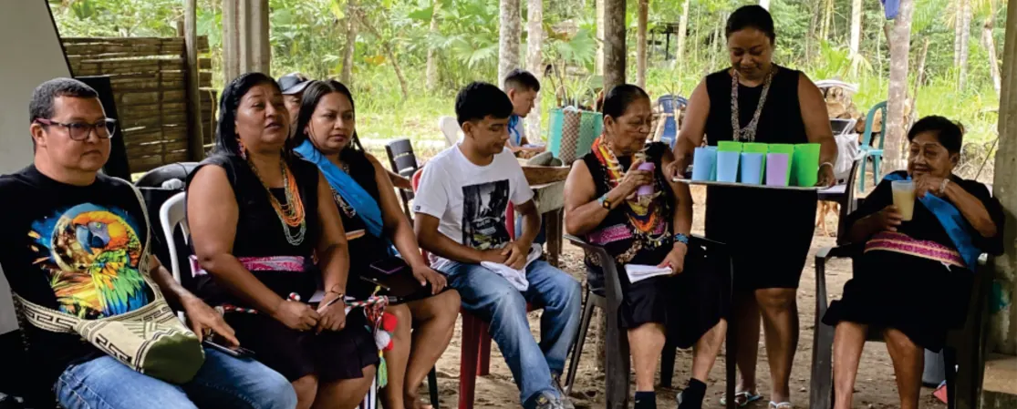Jóvenes y mujeres sentados en una reunión, con traje propio y banda azul.