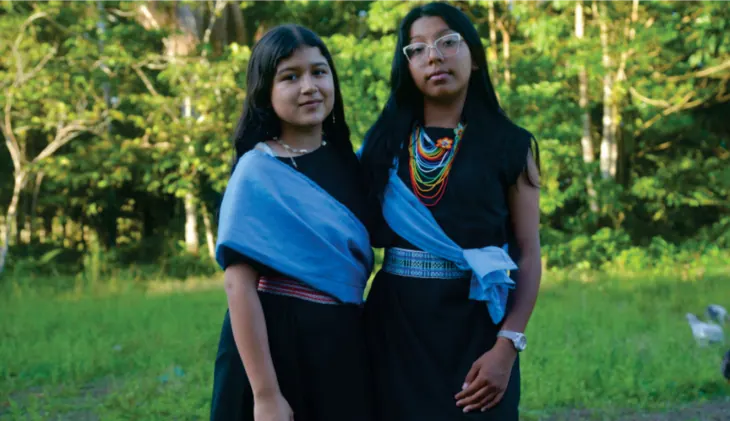 Dos jóvenes mujeres con traje propio y banda azul.