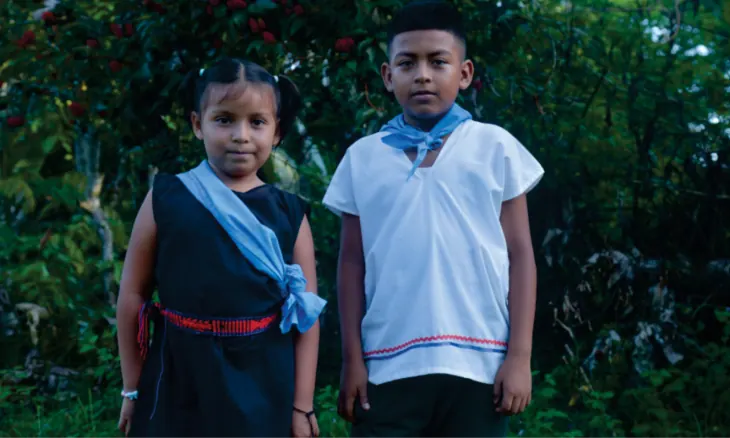 Niña y niño con traje propio y banda azul.