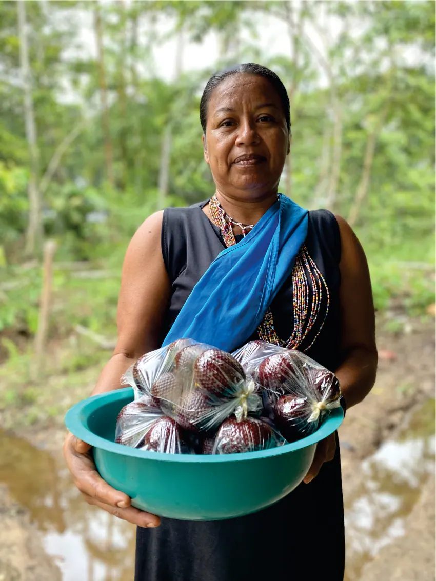 Mujer con traje propio y banda azul que sostiene un recipiente con productos.