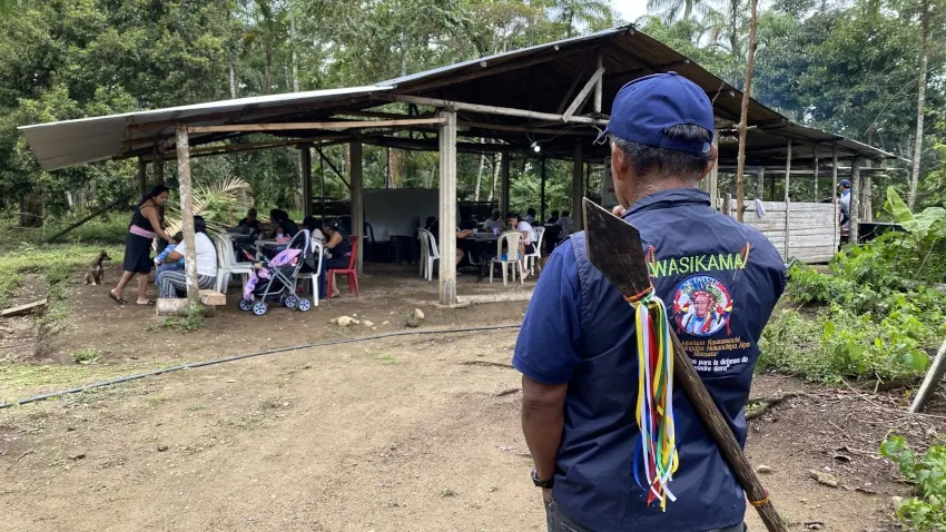 Integrante de la guardia indígena (Wasikama) de espaldas, con bastón, frente a la caseta donde se reúne la comunidad (registro fotográfico).