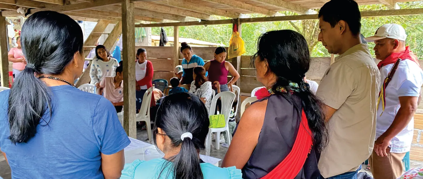 Reunión bajo techo: mujeres y hombres sentados conversando; en primer plano una niña de espaldas.