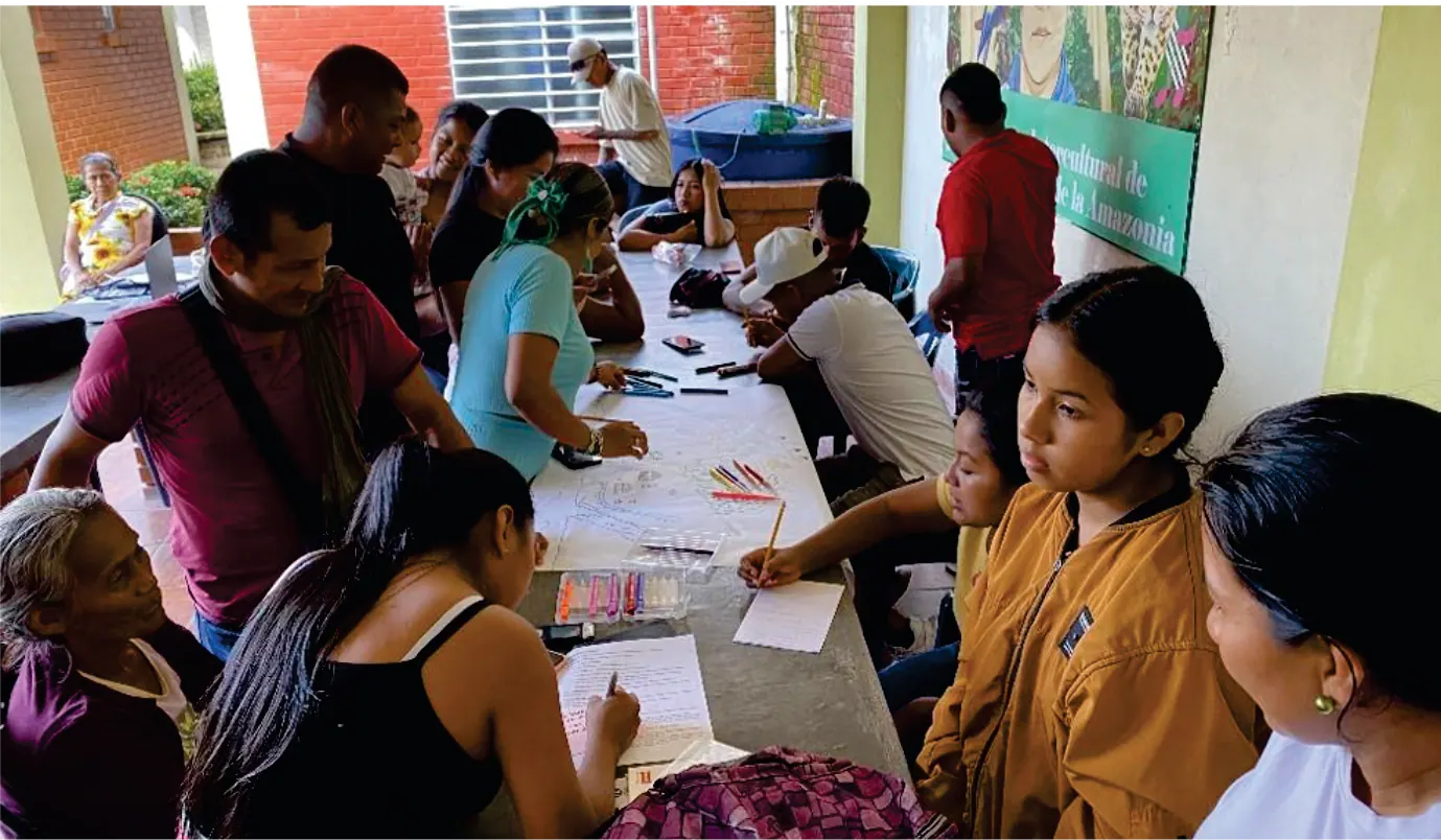 Taller alrededor de una mesa larga: jóvenes y adultos escribiendo sobre papeles.