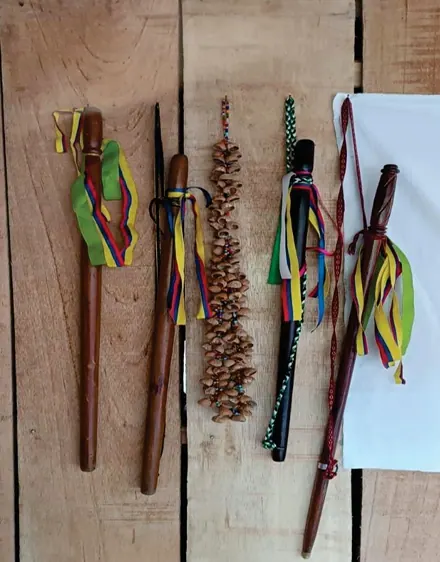 Instrumentos y bastones tradicionales de madera con cintas de colores y un sonajero, sobre una tabla.