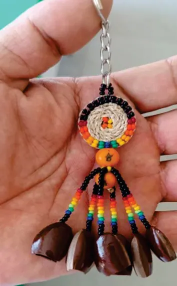 Mano sosteniendo un llavero artesanal de chaquira de colores con semillas colgantes.