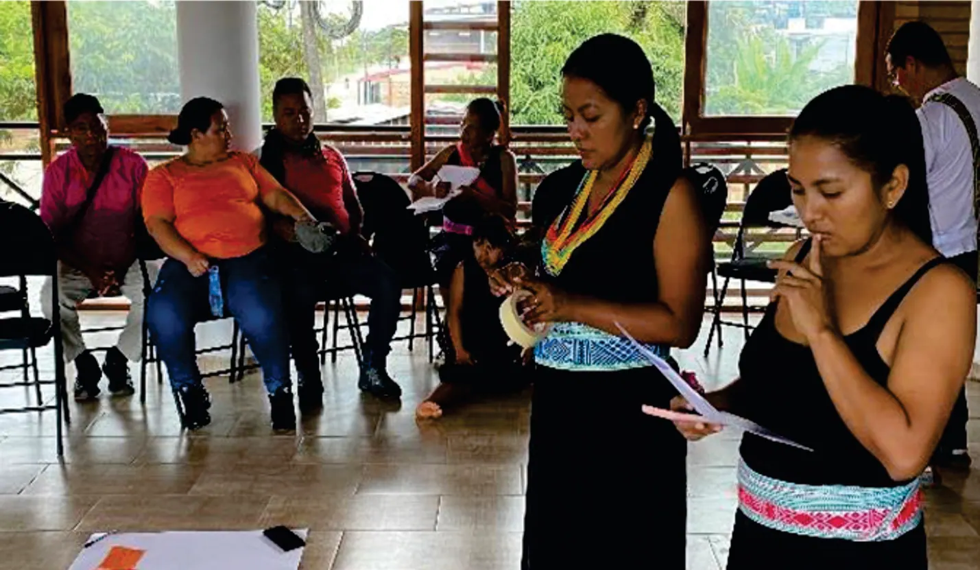 Mujeres jóvenes con traje tradicional de pie, leyendo y exponiendo en un salón.