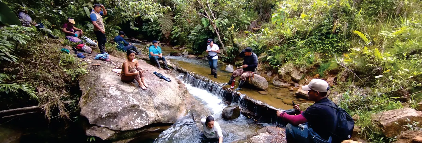Personas sentadas sobre rocas en una quebrada en medio del bosque.