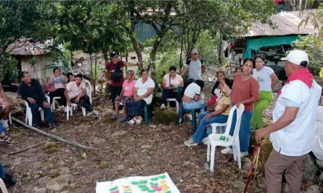 Reunión al aire libre con personas sentadas en sillas en círculo y un mapa extendido en el suelo.
