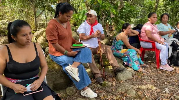 Mujeres y un mayor con pañoleta roja sentados sobre piedras en el monte.