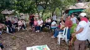 Reunión al aire libre con personas sentadas en sillas en círculo y un mapa en el suelo.