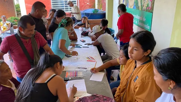 Taller alrededor de una mesa con jóvenes y adultos escribiendo.