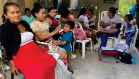 Mujeres sentadas con niños pequeños en una reunión.