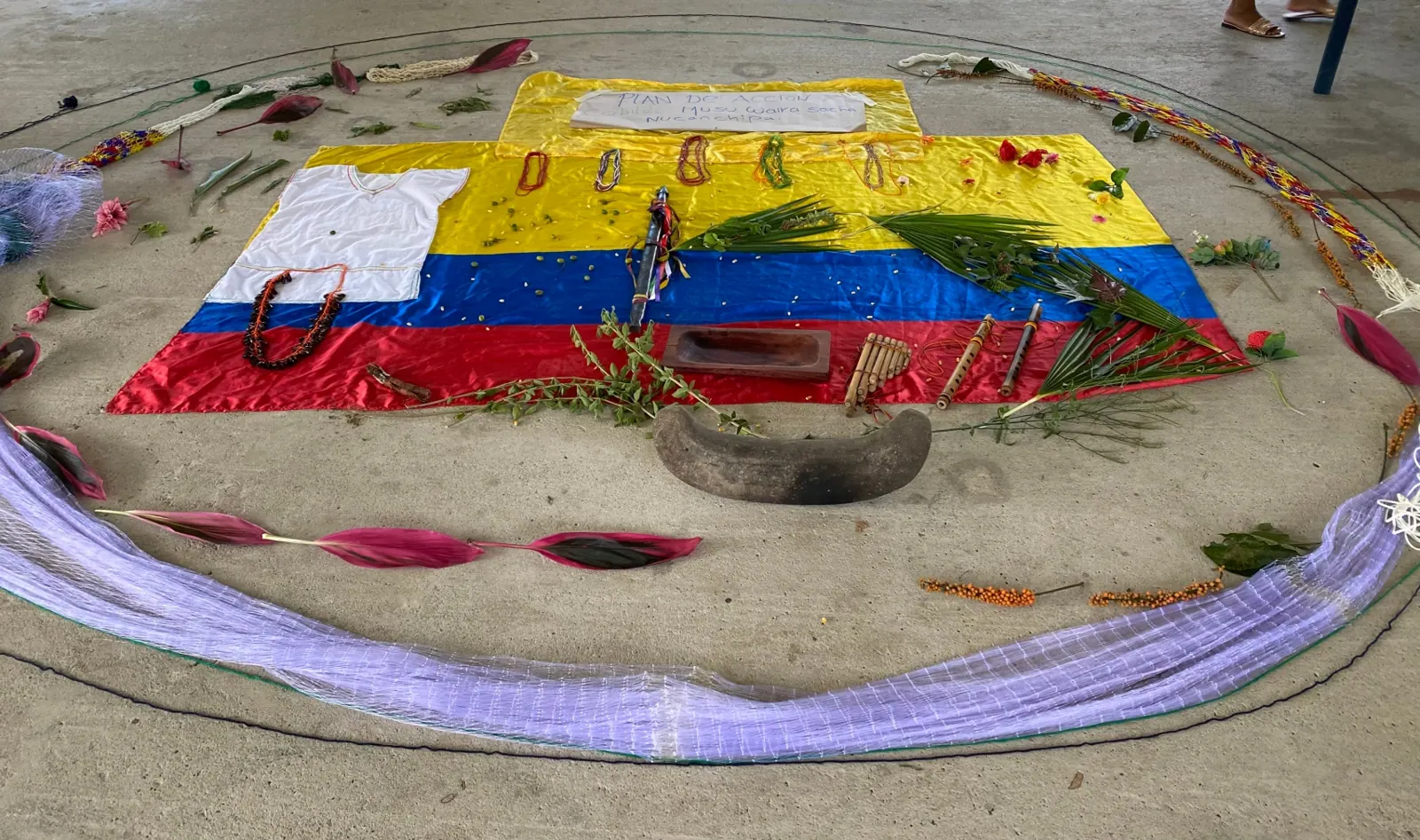 Bandera de Colombia y tejidos extendidos en el suelo con ofrendas, rodeados por un círculo de tela.